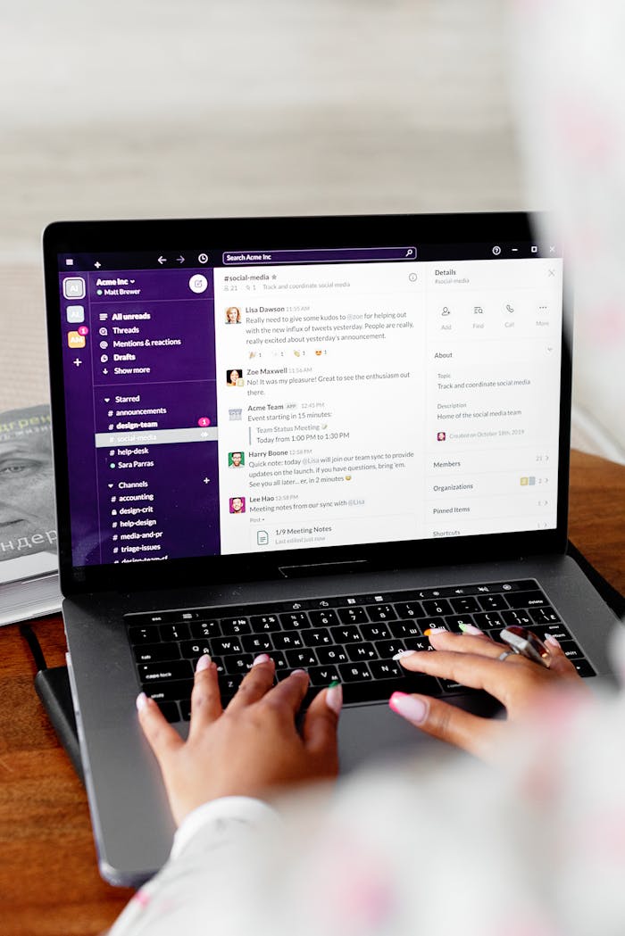 Close-up of hands typing on a laptop displaying Slack for remote communication.